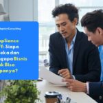 Dua profesional bisnis sedang berdiskusi dan meninjau dokumen di meja kantor sebagai bagian dari proses compliance staff perusahaan.