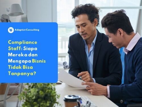 Dua profesional bisnis sedang berdiskusi dan meninjau dokumen di meja kantor sebagai bagian dari proses compliance staff perusahaan.