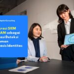 Profesional IT sedang berdiskusi menggunakan tablet mengenai Integrasi SIEM dan IAM sebagai fondasi deteksi ancaman berbasis identitas.