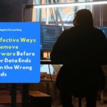 A hacker dressed in dark clothing sits in front of a computer screen displaying red code, remotely launching a spyware attack on the victim’s network of devices.