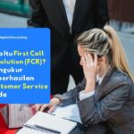 Karyawan yang sedang melayani keluhan pelanggan melalui telpon dan menganalisis data di depan monitor untuk memastikan keberhasilan metrik First Call Resolution (FCR).